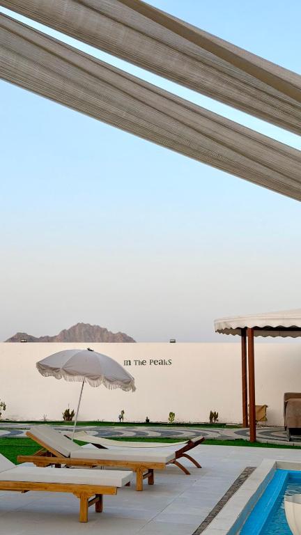 a pool with benches and an umbrella next to a wall at In The Peaks in Sharīyah