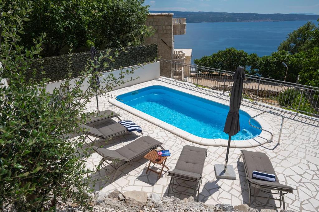a swimming pool with chairs and an umbrella at New Villa OLE, stone house, sea view, jacuzzi in Jesenice