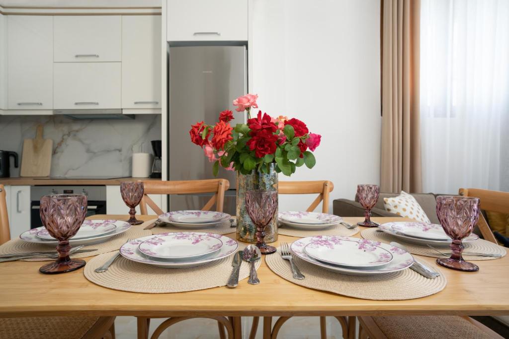 a wooden table with plates and red flowers in a vase at Oasis White Terra in Durrës