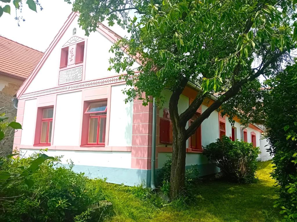 a white house with red windows and a tree at Chalupa Baroko in Mojné