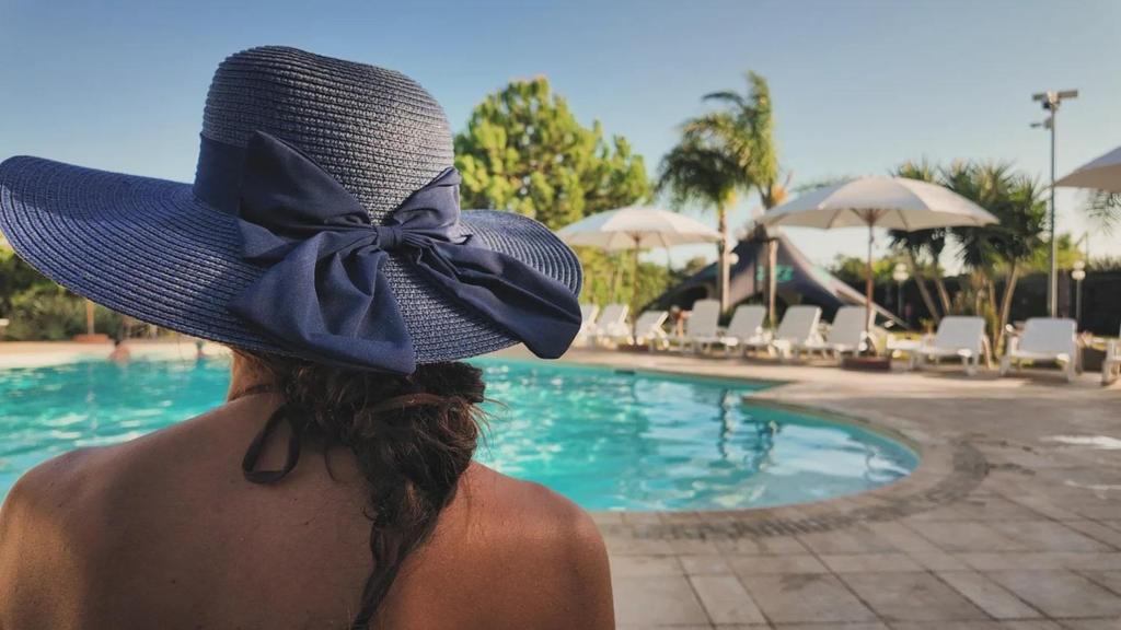 a woman wearing a blue hat next to a swimming pool at Lilybeo Village - Camping & Residence in Marsala