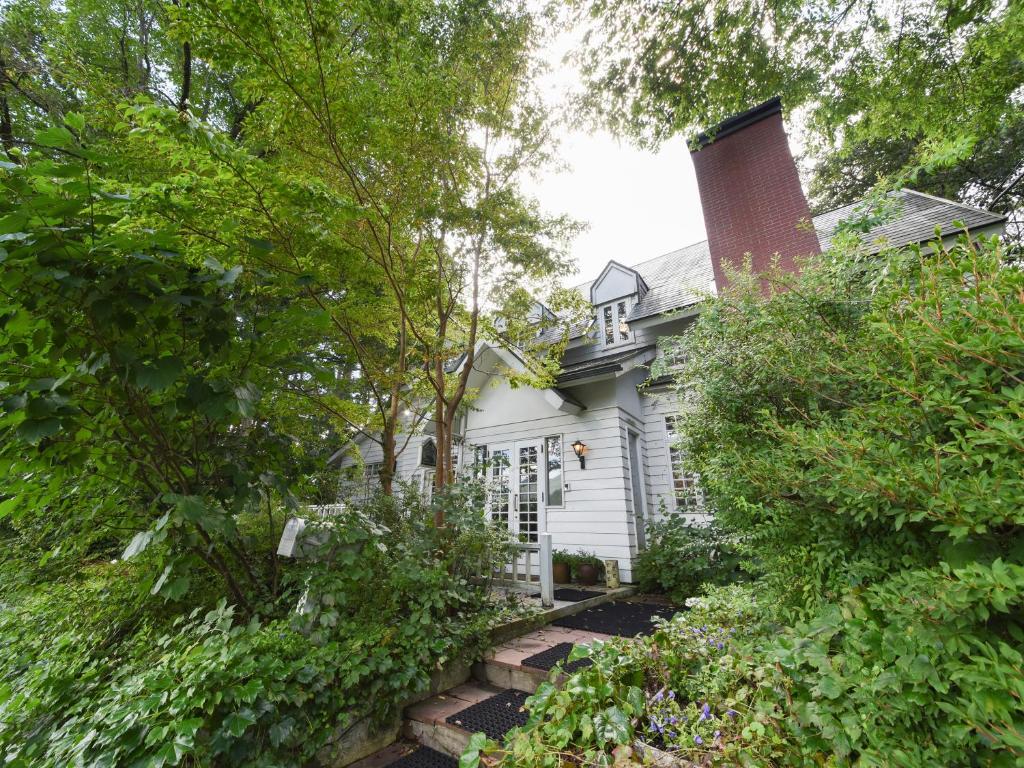 a white house with a brick chimney and trees at Country Inn Orchard House in Hokuto