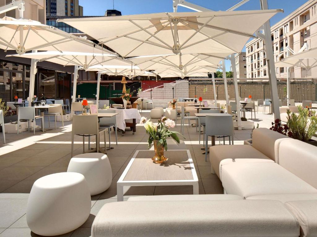 a patio with tables and chairs and white umbrellas at Mercure Montpellier Centre Comédie in Montpellier