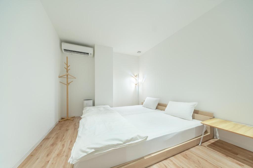 a white bedroom with a white bed and wooden floors at コインズホステル天神ペット宿泊可 in Fukuoka
