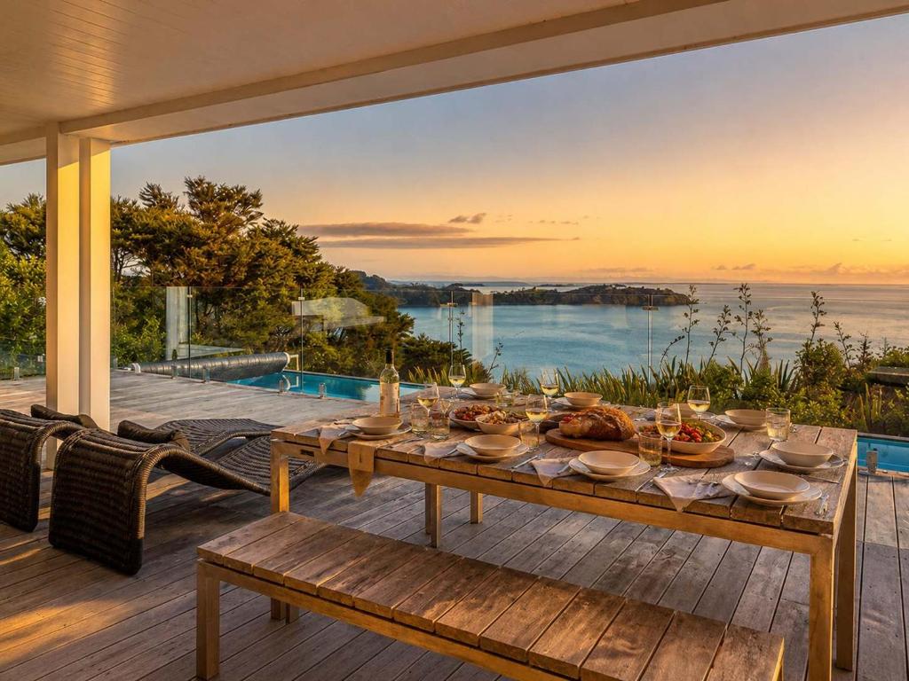 a wooden table with food on a deck with a view of the water at No 63 - Stay Waiheke in Onetangi
