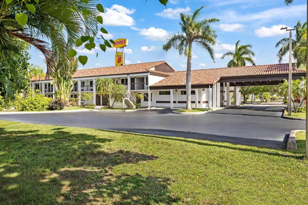 a building with palm trees and a basketball hoop at Super 8 by Wyndham Riviera Beach West Palm Beach in Riviera Beach
