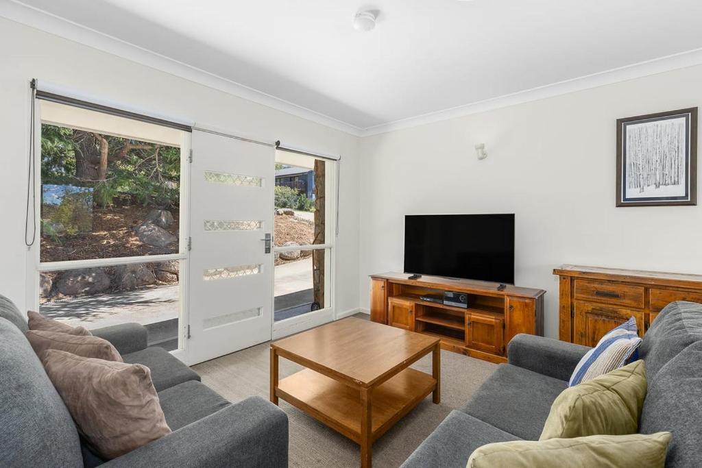 a living room with a couch and a tv at Rock On Cottage in Jindabyne