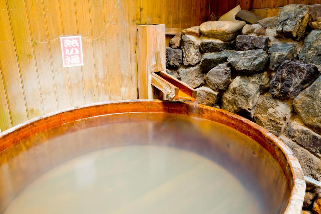 a tub filled with water next to a stone wall at Shibuonsen YAMAICHIYA in Yamanouchi