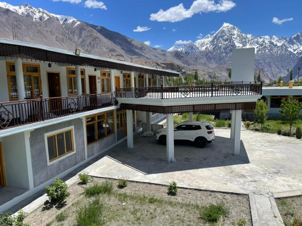 a building with a car parked in a parking lot with mountains at Sost Embassy Hotel By Zeez in Khudābād
