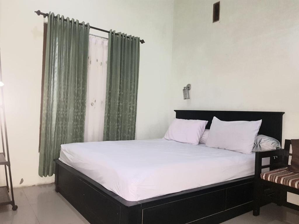 a bedroom with a bed with white sheets and green curtains at Hansel Homestay in Batu