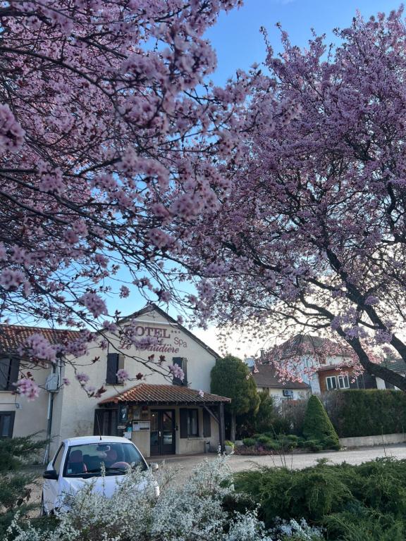 a car parked in front of a house with flowering trees at Maison Legate "Hôtel Le Baudiere & Spa" in Saint-Beauzire