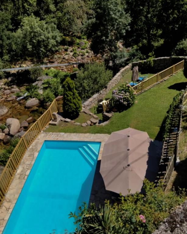 a swimming pool with an umbrella next to a garden at Casas da Peneda - Geres in Gavieira