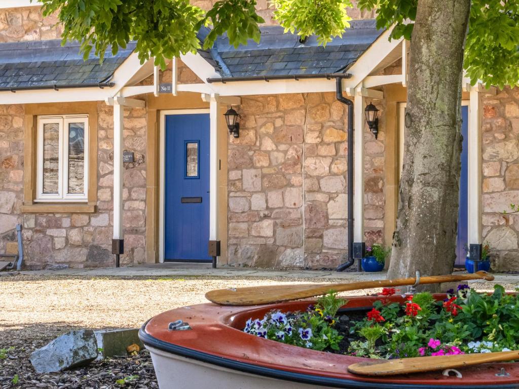 a house with a blue door and a boat with flowers at Smugglers Den in Beadnell