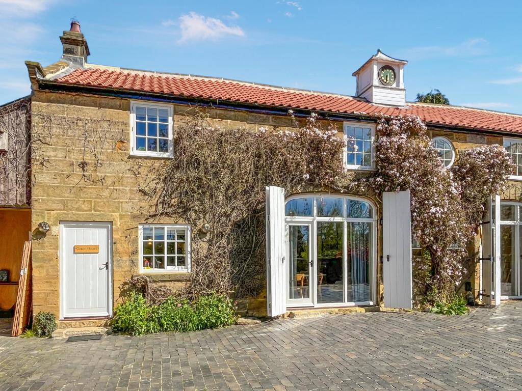 an old stone house with white doors and a clock tower at Coach House - Uk51830 in Great Ayton