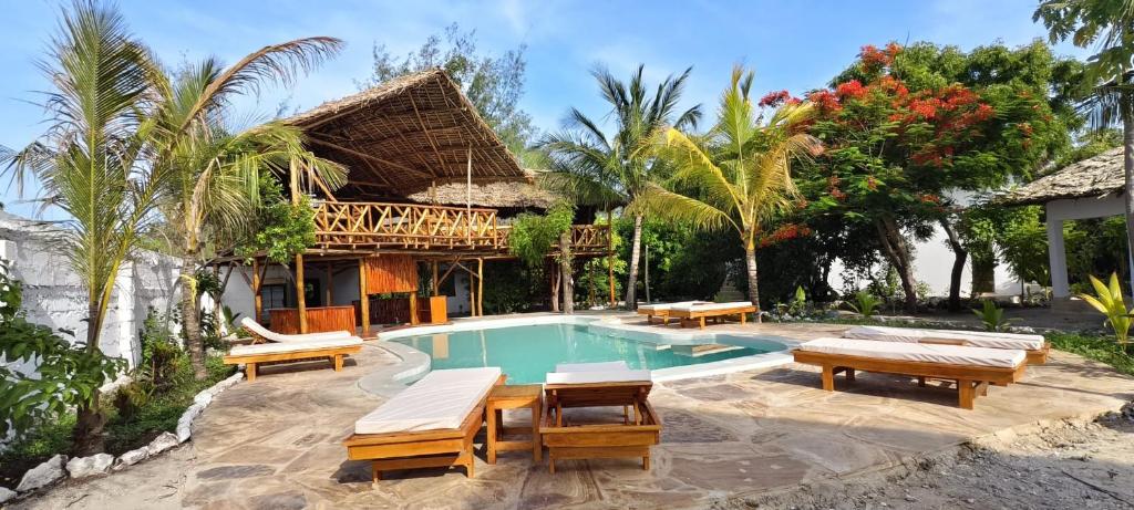 a swimming pool with benches and a house at One Love Garden Villas Paje in Kiganga