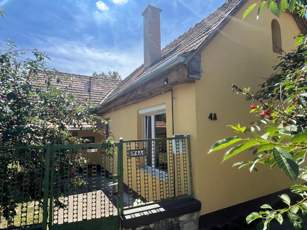 a small yellow house with a gate and trees at Gólyaház in Réde