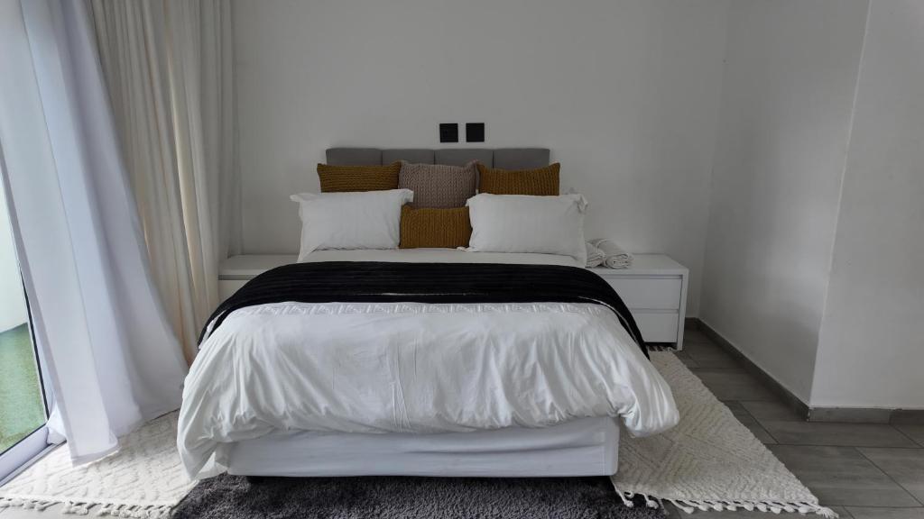 a white bedroom with a bed with white sheets and pillows at Lora Gardens in Chartwell