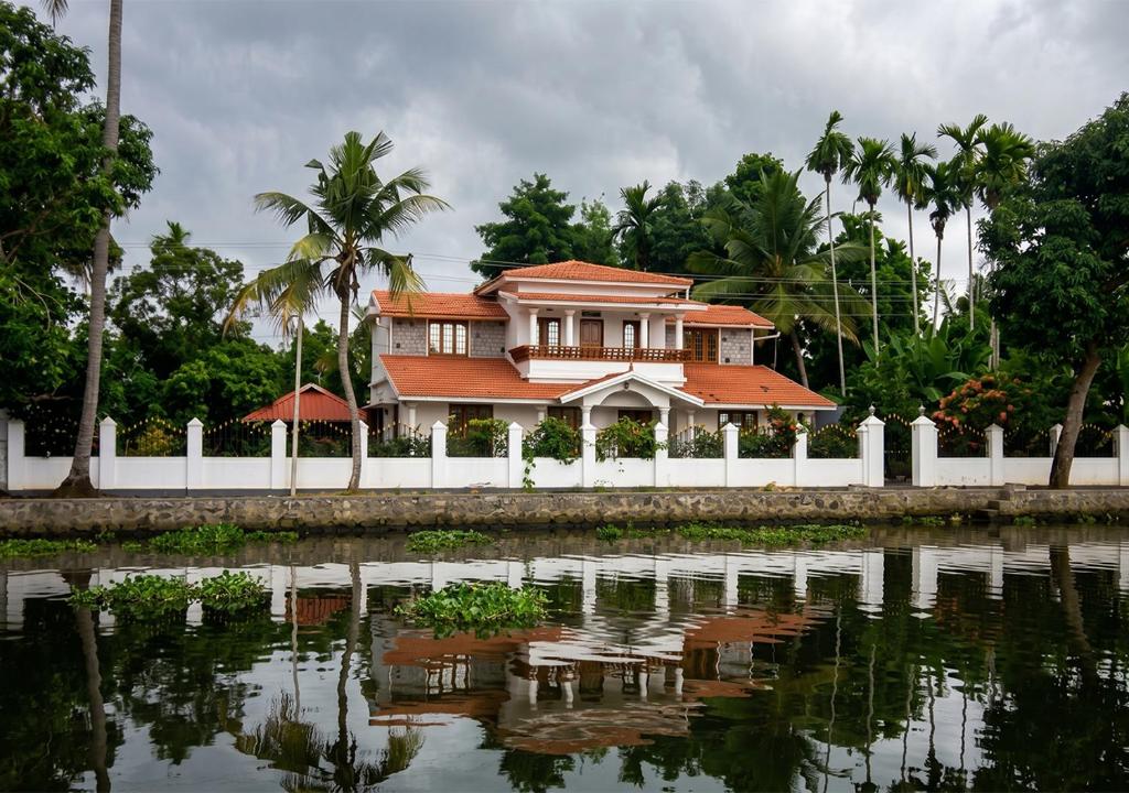 a house with a white fence next to a body of water at VJ Riverfront Villa in Champakulam