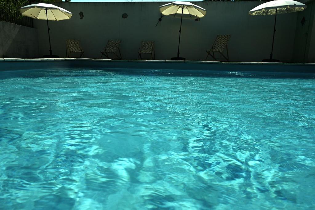 a pool of blue water with chairs and umbrellas at Les Mourguettes in Tulette