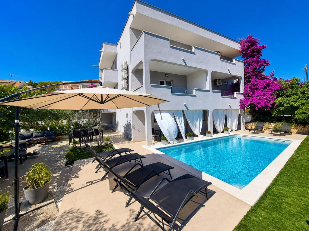 a villa with a swimming pool with chairs and an umbrella at Paulina Harmony Rooms in Seget Vranjica
