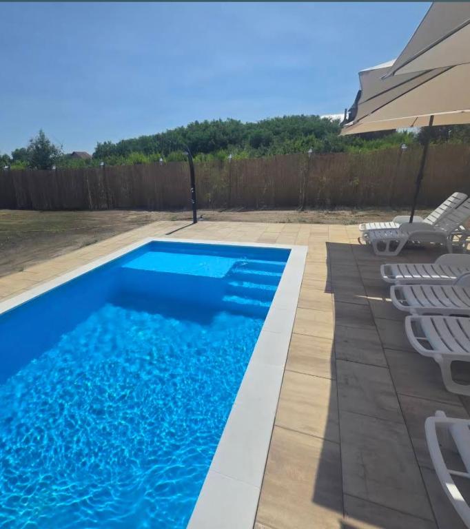 a swimming pool with chairs and an umbrella at Villa Sunset in Palić