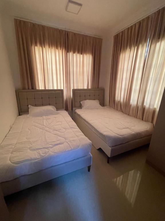 two beds in a room with windows and curtains at شقق مفروشة in ‘Awqad Bayt Marhūn