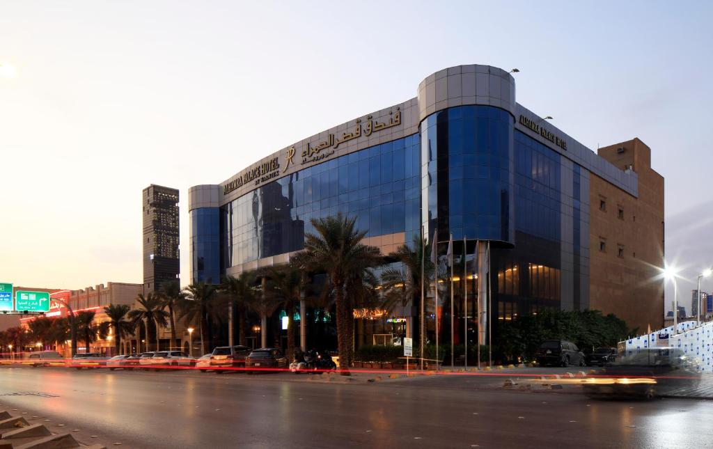 a large glass building with palm trees in front of a street at Qaser Alhamra Hotel Riyadh in Riyadh