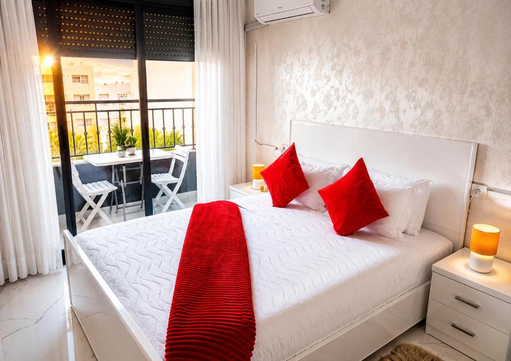 a bedroom with a bed with red pillows and a balcony at Nador Skyline Al Matar in Nador
