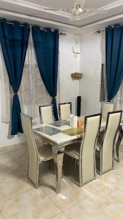 a dining room table and chairs with blue curtains at New ACROPOLE in Komé