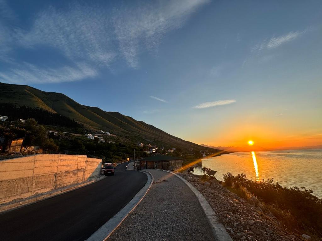 a road next to a body of water with a sunset at Gezim guest house in Shirokë