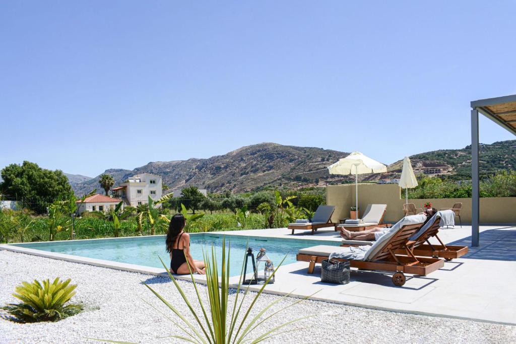 a woman sitting next to a swimming pool at Villa Emanouill Nopigia in Kissamos