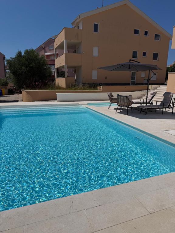 a swimming pool with chairs and an umbrella next to a building at Ventana Pool Apartments - Stara Novalja in Stara Novalja
