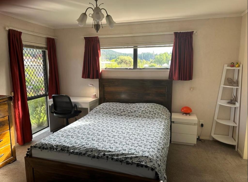 a bedroom with a bed and a desk and windows at Peaceful BnB in Rotorua