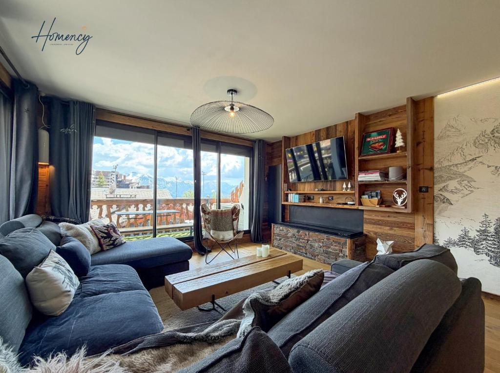 a living room with a blue couch and a large window at Homency - Résidence Ménandière V2 spot in L'Alpe-d'Huez