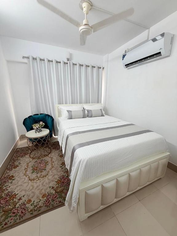a white bedroom with a large bed and a chair at Havene 11 in Dhaka