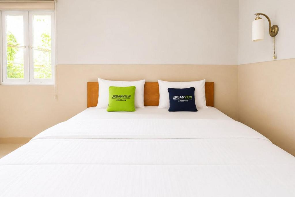a white bed with two green pillows on it at Urbanview Hotel RDN Oasis Cisarua by RedDoorz in Brujul