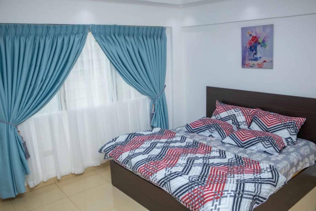a bedroom with a bed with blue curtains and a window at Mycom Apartment in Kumasi