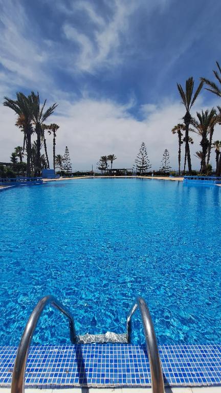 a large swimming pool with blue water and palm trees at Piscine, plage et relaxation in Pont Blondin