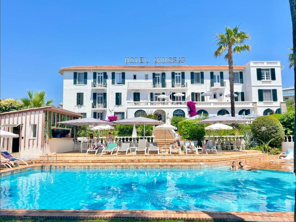 a hotel with a swimming pool in front of a building at Hotel des Mimosas in Juan-les-Pins