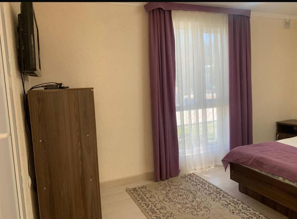 a bedroom with a bed and a window with purple curtains at Дом у Айбека in Tamga