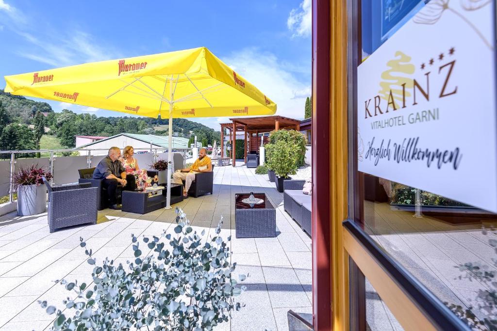 a patio with a yellow umbrella and people sitting at tables at Vital Hotel Krainz mit Nebenhaus Familien Hotel in Loipersdorf bei Fürstenfeld