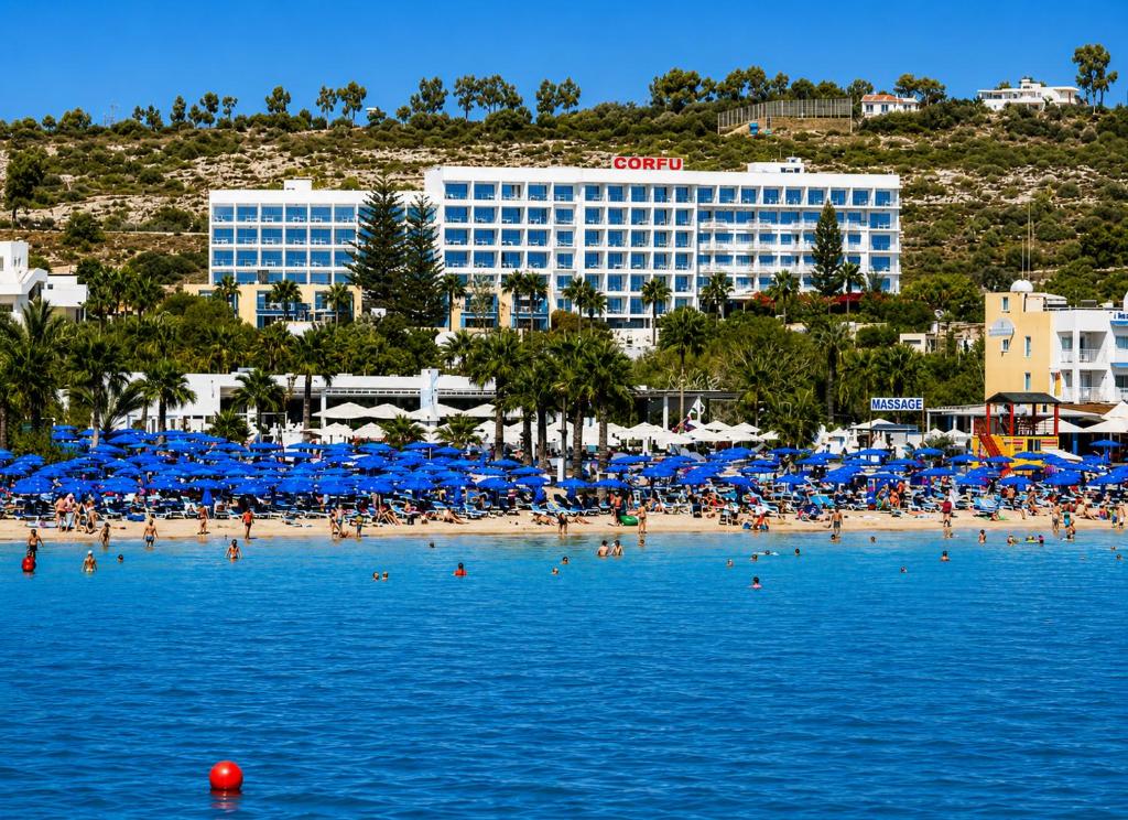 a group of people on a beach with blue umbrellas at Corfu Hotel in Ayia Napa