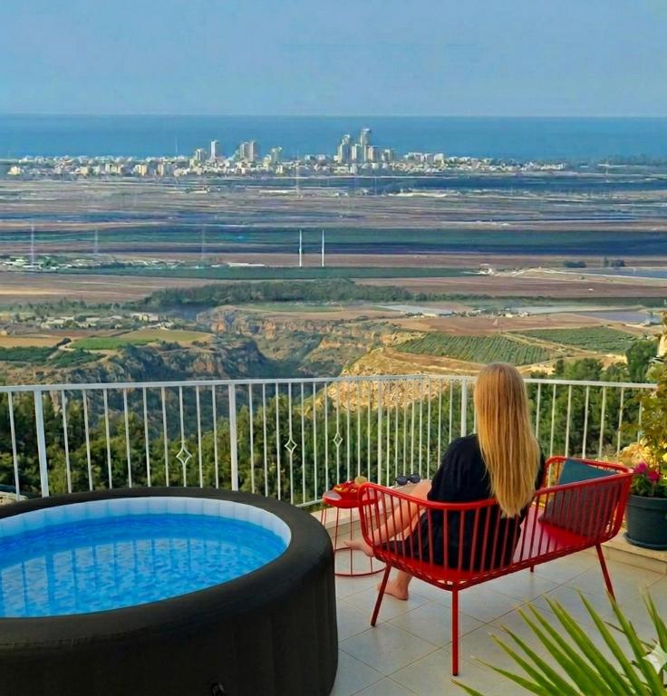 a woman sitting in a red chair looking out at the city at מול הים in Moreshet