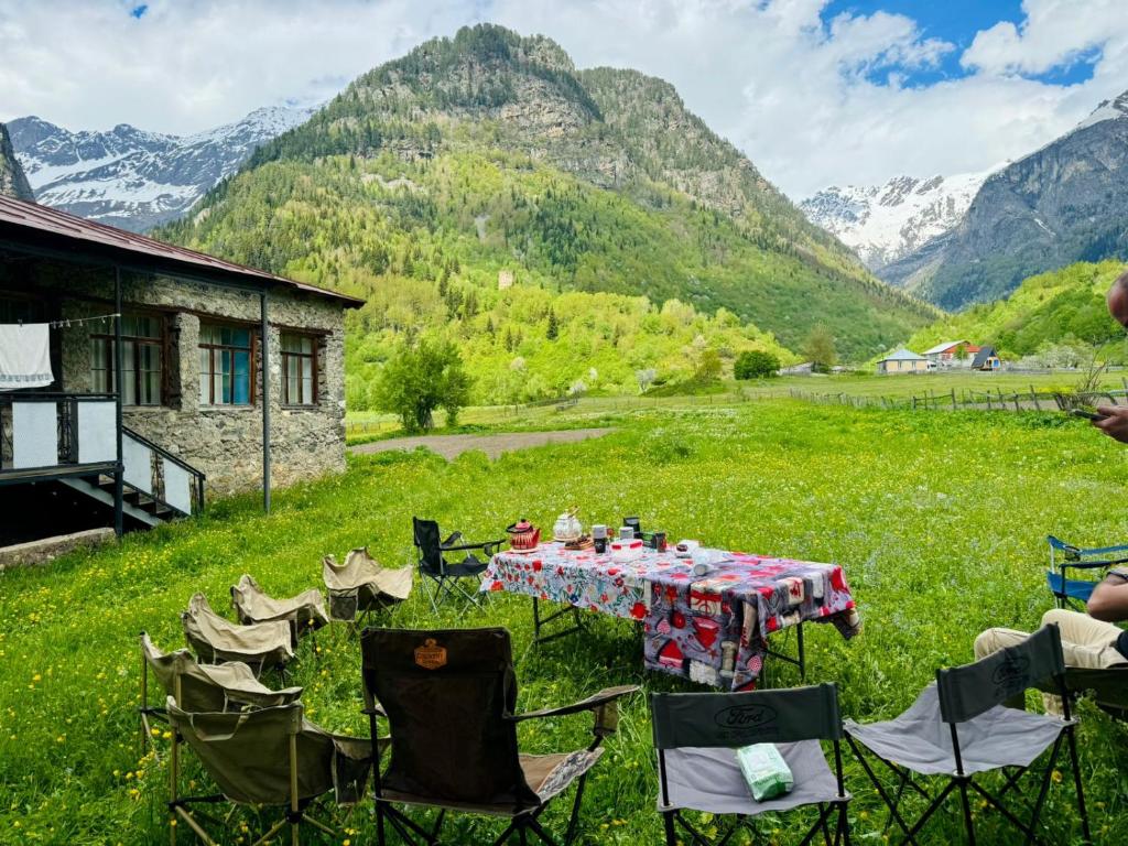 a table and chairs in a field with mountains in the background at Madisha's Guesthouse in Mestia