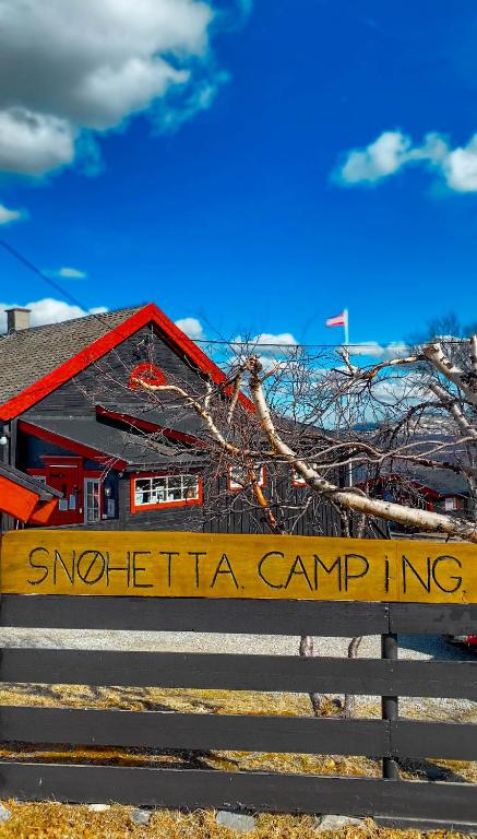 a sign in front of a red building with a house at Snøhetta Camping in Hjerkinn