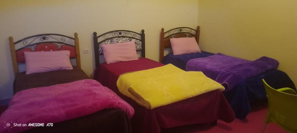three beds with colorful covers in a room at Camping Imdghas in Tilmi