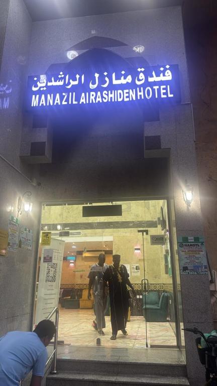 two people walking into a building with a sign at فندق منازل الراشدين in Az Zahrāʼ