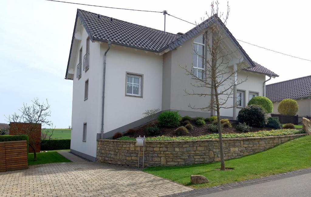 a white house with a stone retaining wall at Ferienwohnung Hansen in Welschbillig