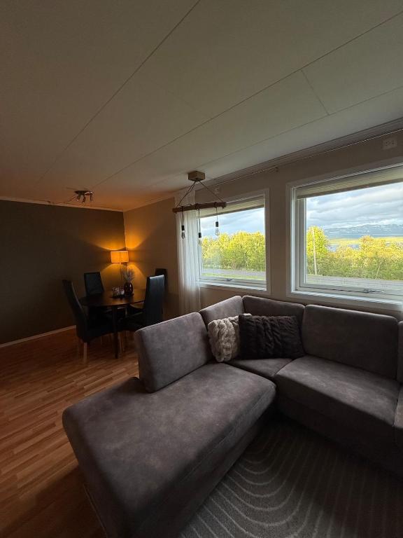 a living room with a couch and a table and two windows at Cozy apartment with two bedrooms in Tromsø