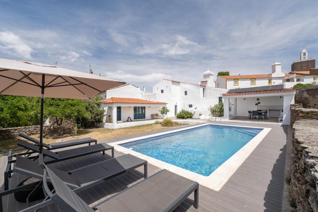 a pool with chairs and an umbrella and a house at Casa do Loureiro in Alandroal